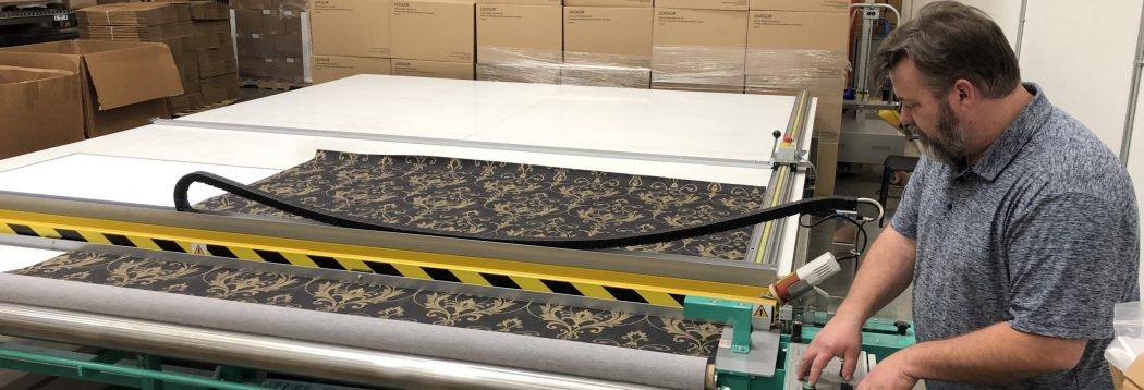 A fabricator guiding patterned fabric through a cutting table on a window treatment production floor.