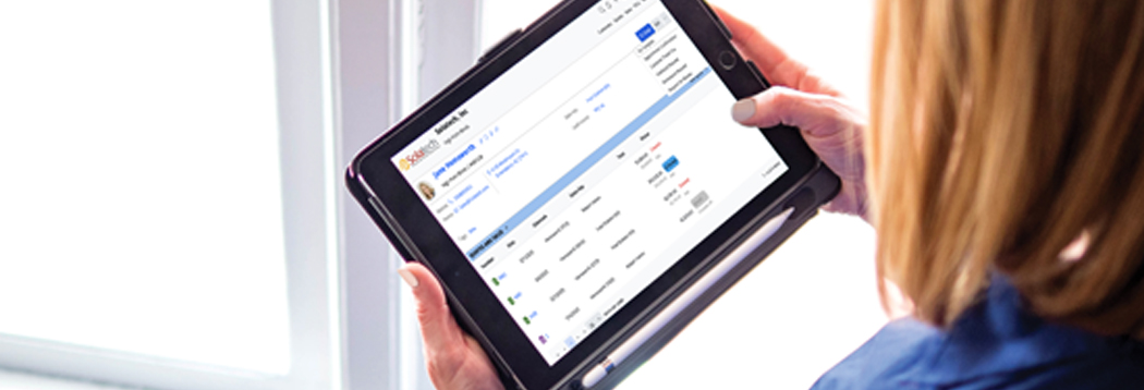 A window covering professional reviewing a job in Solatech Focus on a tablet beside a sunlit window.